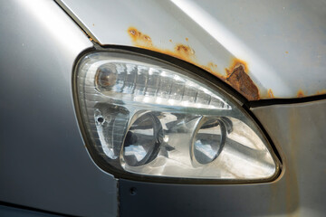 old defocused headlight on a gray rusty car body.
