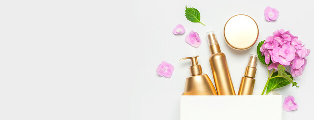 Cosmetic mock up gold bottles. Cosmetics, white gift bag, pink hydrangea flowers on light background. Cosmetics springtime summer Concept. Flat lay top view. Branding products, spa, beauty background