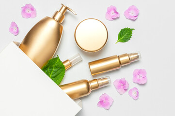 Cosmetic mock up gold bottles. Cosmetics, white gift bag, pink hydrangea flowers on light background. Cosmetics springtime summer Concept. Flat lay top view. Branding products, spa, beauty background