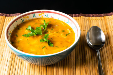  SOUP WITH VEGETABLES IN A BLUE DISH CONTAINER ON A SMALL STRAW POT