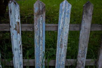 Old dilapidated wooden fence with paint on the background of green grass. The concept of simple rural life. Village background.