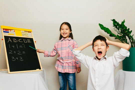 Little girl teaching a boy, he is screaming. Funny situation in classroom. Home education in Central Asia, lesson for kids