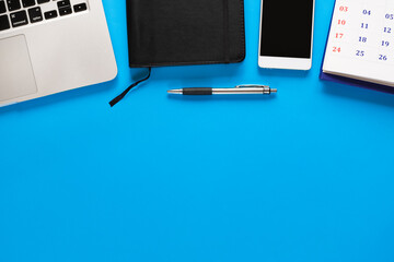 Top view of laptop, notebook, smartphone, and calendar on blue background.