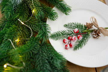 Greeting card. Wooden table with christmas decoration. Table setting with utensils. Festive decoration of fir branches and garlands. Interior Design
