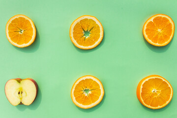 Bright, tasty, fresh, juicy orange slices with an apple slice on green background, natural vegan food, good for alphabet, vitamins for immune system