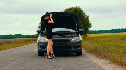 A young girl in a short dress opens the hood of a broken car . The car suddenly broke down on a country road down while driving.	
