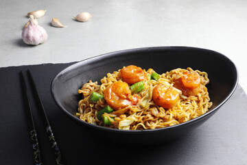 The instant noodles yakisoba are cooked dry and served in the black bowl and the black holder on the grey table