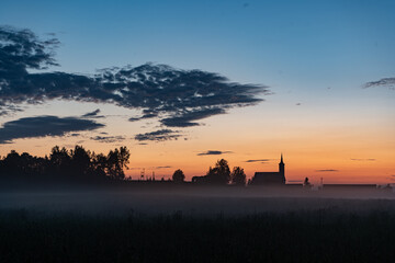 Old catholic church building with nature landscape. Amazing sunset with fog over the field.