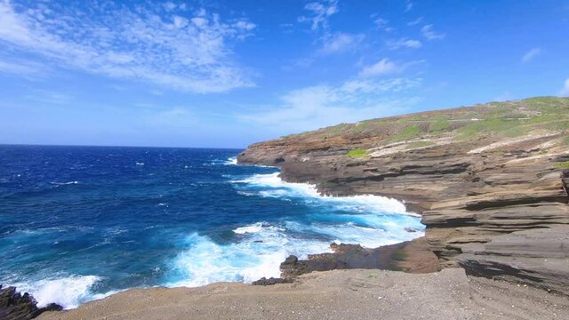 Pacific Ocean waves hitting into rocky coast of Hawaiian island Oahu. Big volcanic rocks with blue sunny sky.