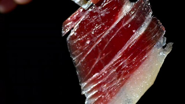 Incredible image of a slice of Iberico ham, that moves with the wind and is shown to the camera in a short image detail. Very appetizing to eat that delicacy, with impressive red and white colors