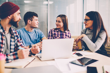 Cooperation of young people in casual wear on design project during brainstorming meeting in modern office.Male and female employees discussing creative idea for startup sitting at table with laptop