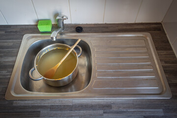 A dirty pot with a wooden spoon in in a kitchen sink.