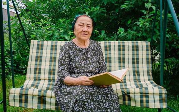 Portrait of an old Asian woman realing a book in her garden, smiling and feeling happy