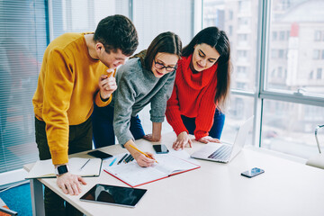 Collaboration of young professionals on creating design of new project in office.Team of successful hipster students dressed in casual wear cooperating on common studying task during brainstorming
