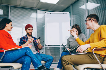 Group of millennial hipster students dressed in casual wear discussing website and app using modern technology and wireless internet during courses in classroom with flip chart with mock up area