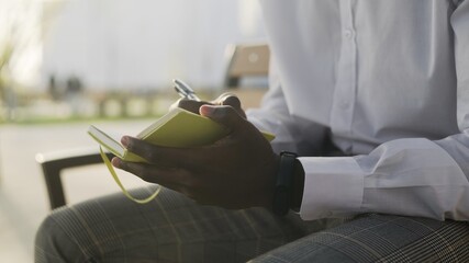 Young African American Man on a bench at the park writes her thoughts in a diary