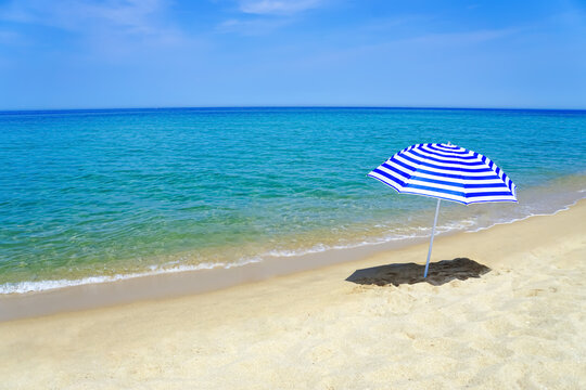 Striped blue and white sun umbrella on a white sand beach with emerald water. Sea landscape.      