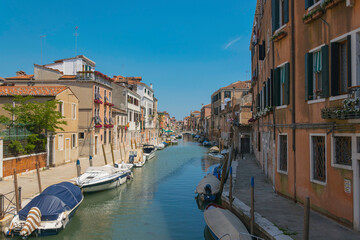 canal in venice italy, with docked boats, old houses and clear sky