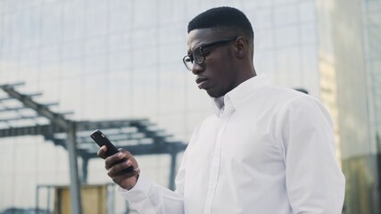 Attractive African Businessman with smart phone chatting online outdoors