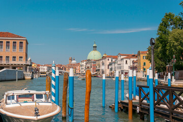 Grand canal in Venice, Italy, with dock for boats and gondolas with colorful poles. Ancient buildings in the background