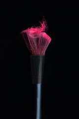 Make-up brush with pink powder isolated in a black background
