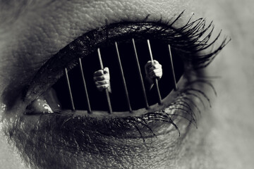 Conceptual monochrome photo of hands holding the bars of a prison inside human eye - 359936325