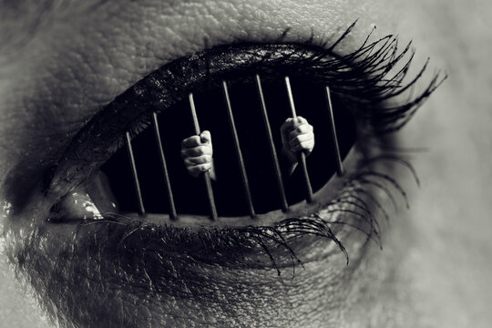 Conceptual monochrome photo of hands holding the bars of a prison inside human eye