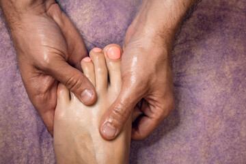 Closeup photo of chiropractor or masseur hands massaging anonymous woman’s toes and foot