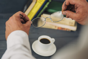Concept on the topic of education. A man with glasses reads books, on a wooden background with coffee.
