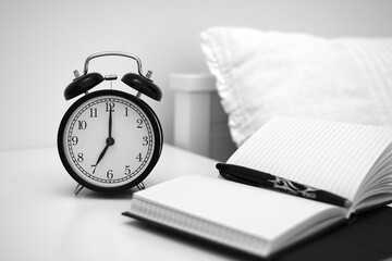 Alarm clock on table with notebooks and pen. Wake up concept. An image of alarm clock showing 07:00...