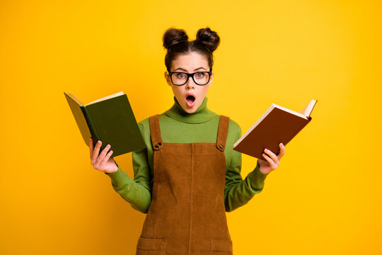 Portrait of her she nice attractive stunned wondered knowledgeable girl nerd reading two book compare preparing test isolated bright vivid shine vibrant yellow color background