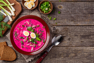 Cold beetroot soup with cucumber, greens, quail eggs in a bowl on a wooden table. Rustic style. Top view. Copy space 