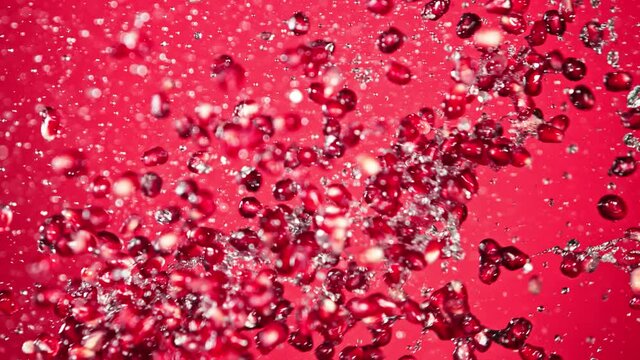 Super Slow Motion Shot of Fresh Pomegranate Seeds and Water Side Collision on Red Background at 1000fps.