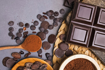 Chocolate bar and drops, cocoa beans and powder on grey background
