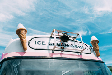 Ice cream cone with a pink retro ice cream truck or van in the background. High quality photo. Summer vibes in pastel colours. 