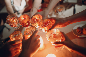 Hands holding the glasses with drink making a toast at party. Soft focus and burning candle in background