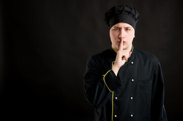 Young male dressed in a black chef suit showing shh gesture