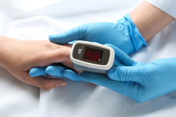 Doctor examining patient with fingertip pulse oximeter in bed, closeup