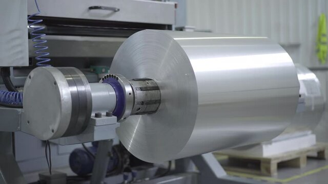 Aluminium foil sheet rolling on industrial equipment. Automated machinery processing raw material on manufacturing site conveyor. Business, industry, production.