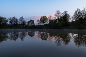 Bäume und Wolken spiegeln sich im Wasser im stimmungsvollen Abenlicht
