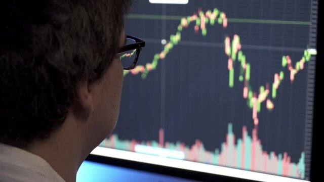 Businessman analyzing a graphic of a stock exchange chart. Back of the head of a young male businessman looking at a stock diagram on the big screen of the computer