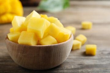 Cubes of fresh ripe mango in bowl on wooden table