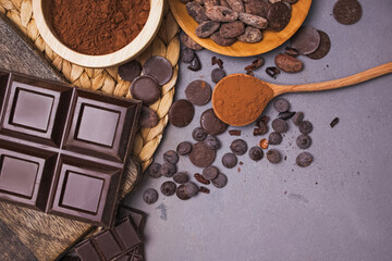 Chocolate pieces and drops, cocoa beans and powder on grey background