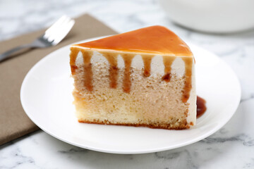 Slice of delicious cake with caramel sauce on white marble table