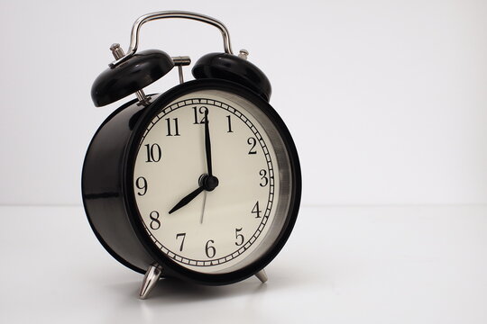 Black vintage alarm clock on table. White background. Wake up concept. An image of a retro clock showing 08:00 pm/am.    