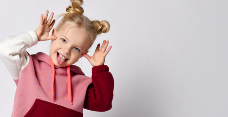 Little blonde lady with buns hairstyle, in colorful sport suit, sneakers. Making faces, showing tongue, posing isolated on white