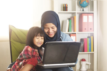 Asian muslim mom and little baby girl daughter learning online or watching videos on laptop, happiness between mother and kid, single parent being happy
