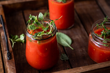 Vegan tomato gazpacho with fresh herbs. Served in glass jars. Rustic, wooden background.