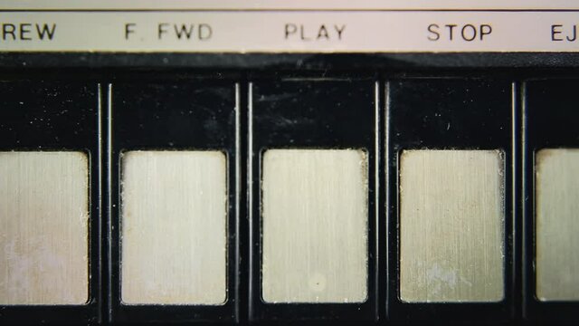 Macro detail shot from above: a finger pressing the play button on a vintage audiocassette player.
