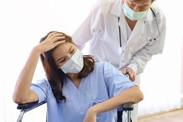 A patient woman wear face mask and sitting on wheelchair and covid-19 emergency treatment in a hospital room, doctors wear uniform protection